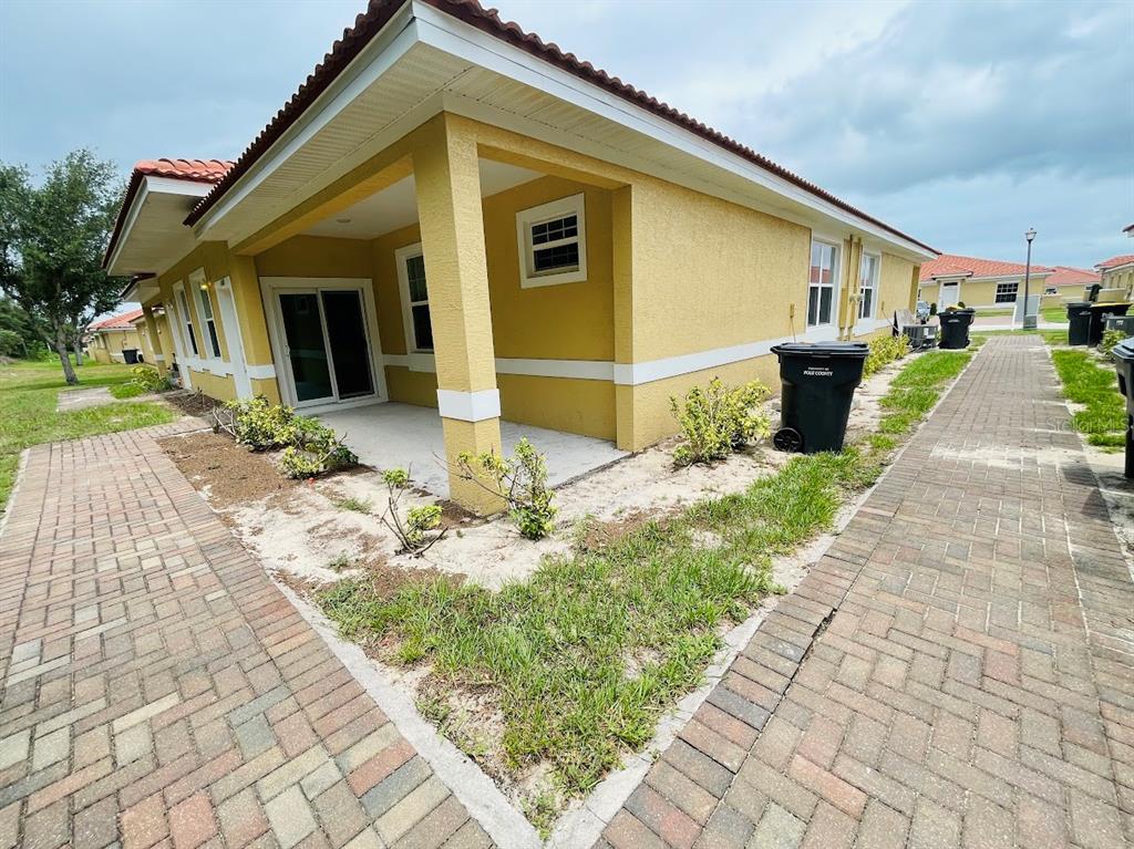 A yellow stucco house exterior features a covered patio, brick walkways, and landscaping — 1601 CUMIN DRIVE, KISSIMMEE, FL