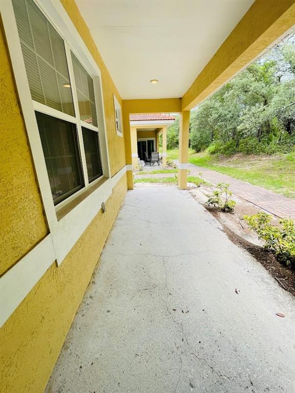 A covered concrete patio runs along the side of a yellow stucco house — 1601 CUMIN DRIVE, KISSIMMEE, FL