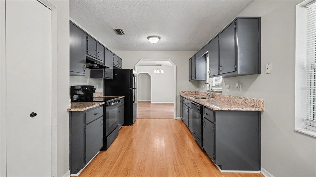 A galley kitchen features dark gray cabinets, granite countertops, and light wood flooring — 4620 NE 8TH STREET, OCALA, FL