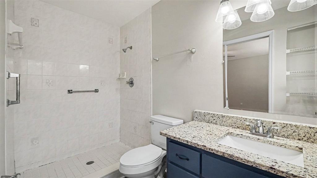 A bathroom features a tiled walk-in shower, a toilet, and a vanity with granite countertops — 4620 NE 8TH STREET, OCALA, FL
