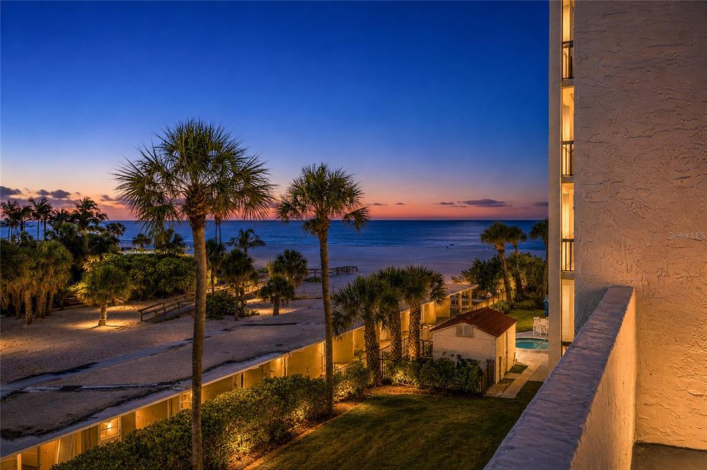 An elevated view of a beach at dusk with palm trees and a building exterior — 1100 BENJAMIN FRANKLIN DRIVE UNIT 305, SARASOTA, FL