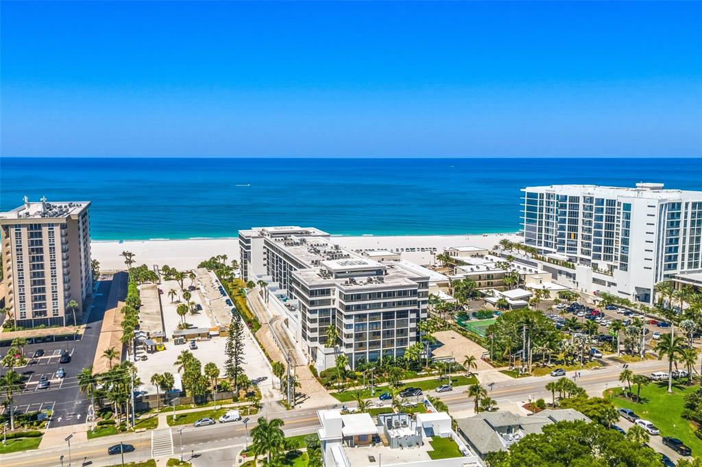 An aerial view shows several beachfront hotel buildings and parking lots along a sandy coast — 1100 BENJAMIN FRANKLIN DRIVE UNIT 305, SARASOTA, FL