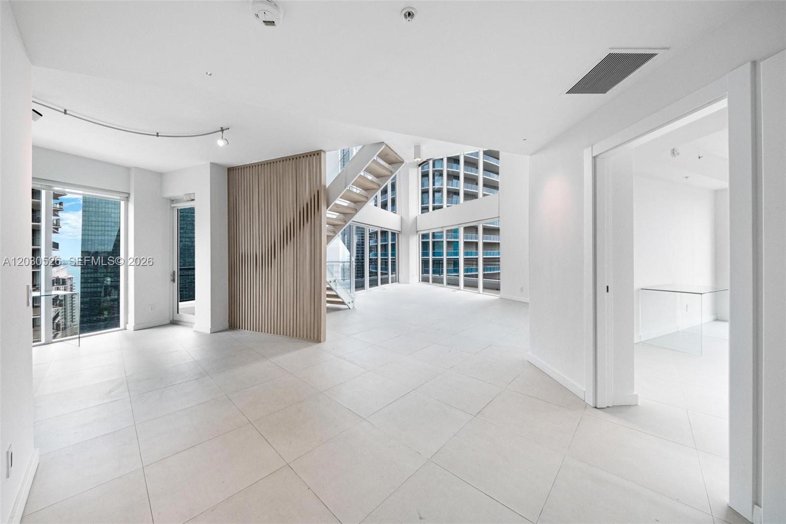 A bright, modern living area features white tile floors, a wooden slat wall, and stairs — 60 SW 13th St # 2600, Miami FL 33130, MIAMI, FL