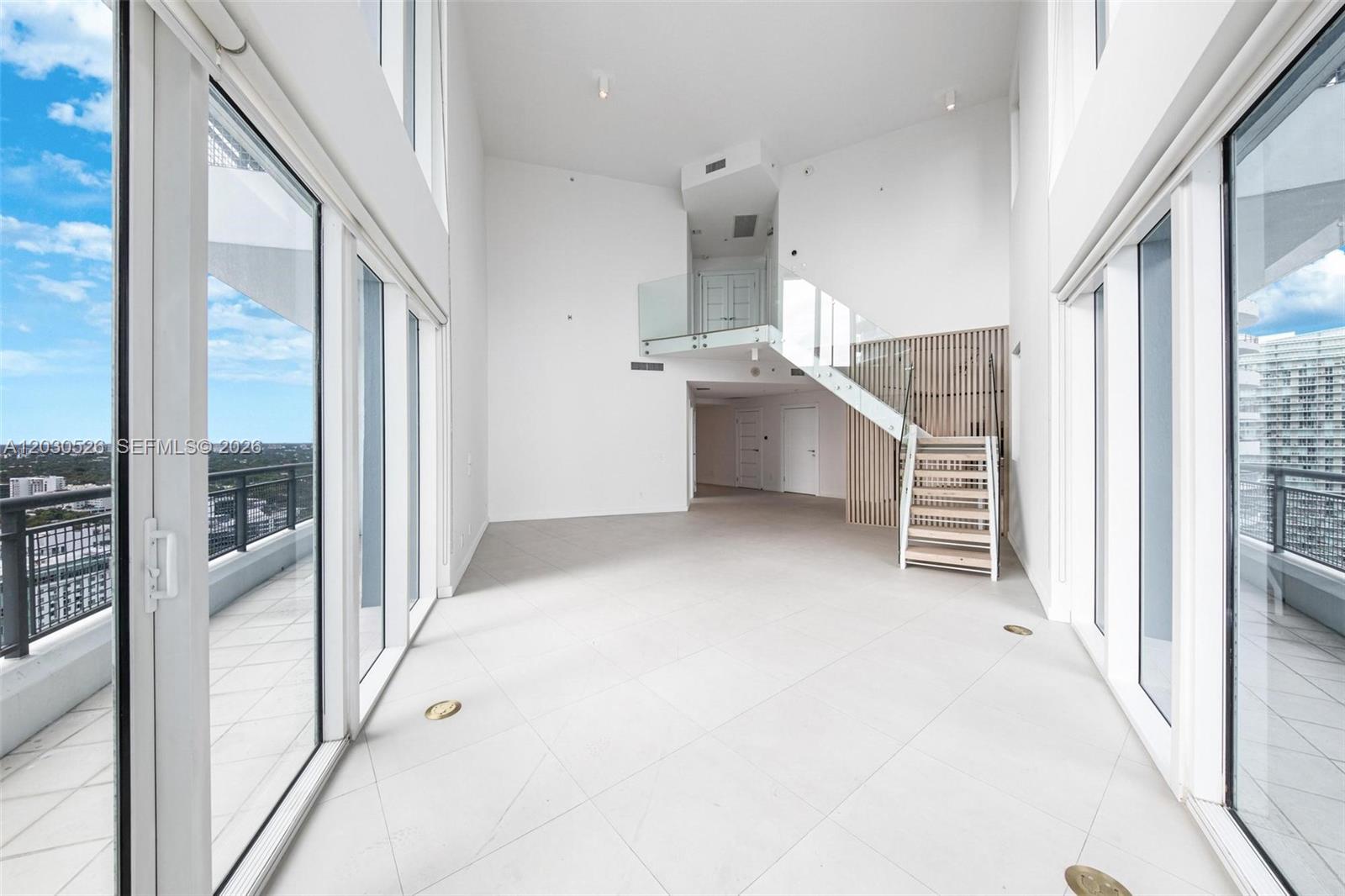 A bright, modern living room features high ceilings, white tile floors, and a glass staircase — 60 SW 13th St # 2600, Miami FL 33130, MIAMI, FL