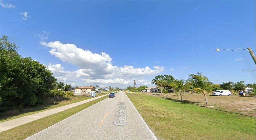 A paved road stretches through a residential area with grassy lots and scattered palm trees — 10420 GULFSTREAM BOULEVARD, ENGLEWOOD, FL
