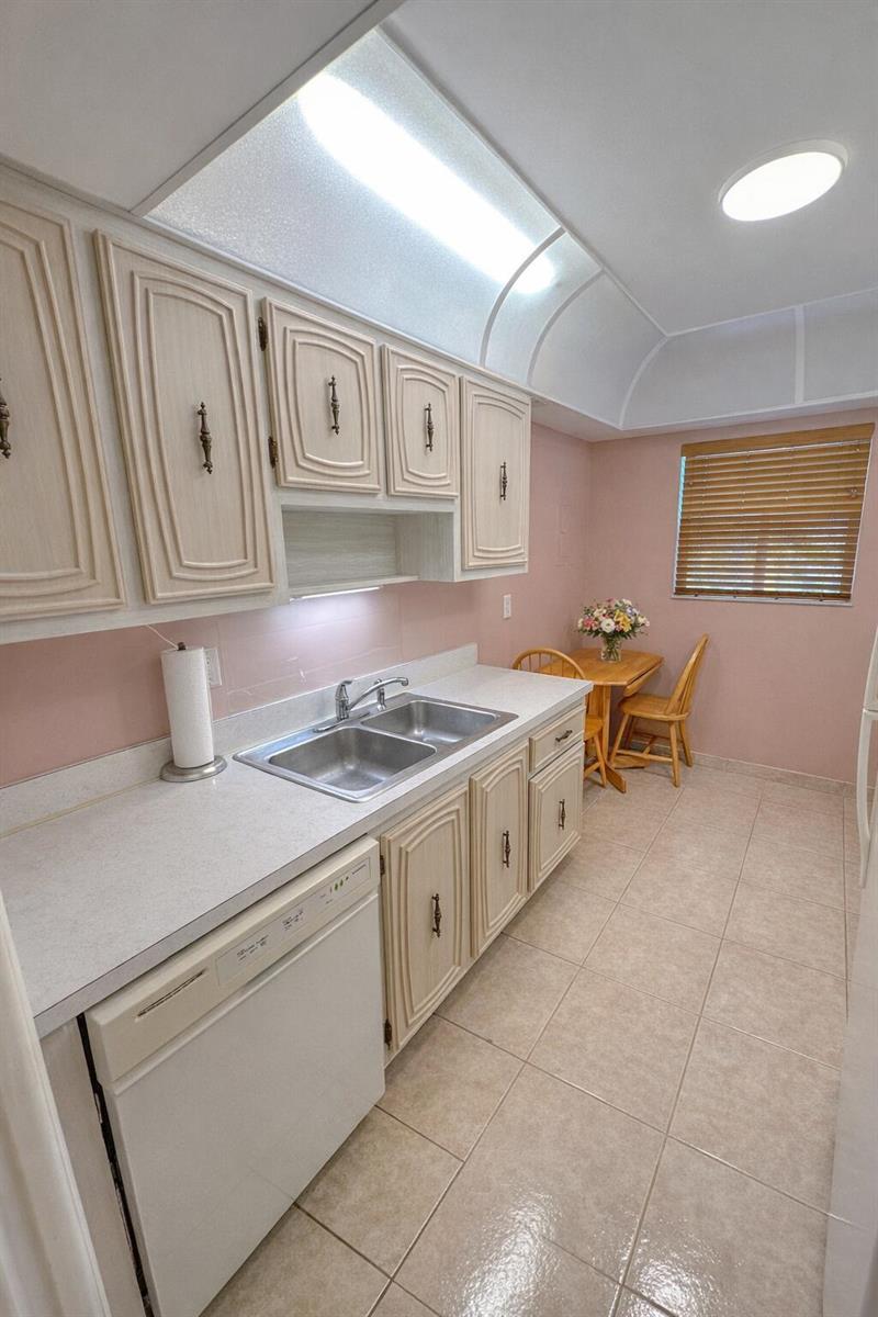 A kitchen features light-colored cabinets, a double sink, pink walls, and a small dining area — 2740 SW 22nd Avenue # 1605, Delray Beach FL 33445, DELRAY BEACH, FL
