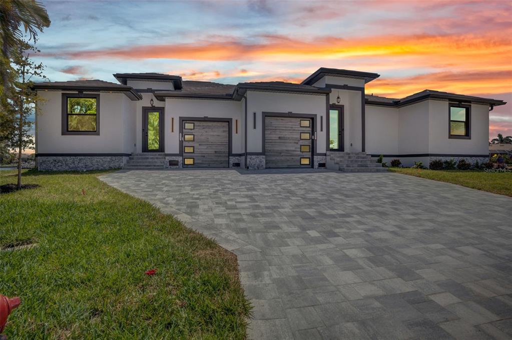 A modern single-story house with a paver driveway, two garages, and white stucco exterior walls — 1327 WESLEY DRIVE, PUNTA GORDA, FL