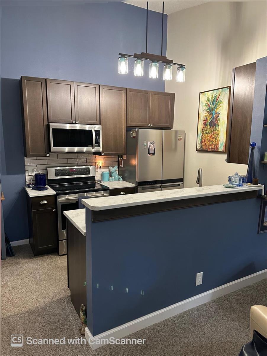 A kitchen features dark wood cabinets, stainless steel appliances, and a blue-painted breakfast bar — 6512 Chasewood Drive # H, Jupiter FL 33458, JUPITER, FL