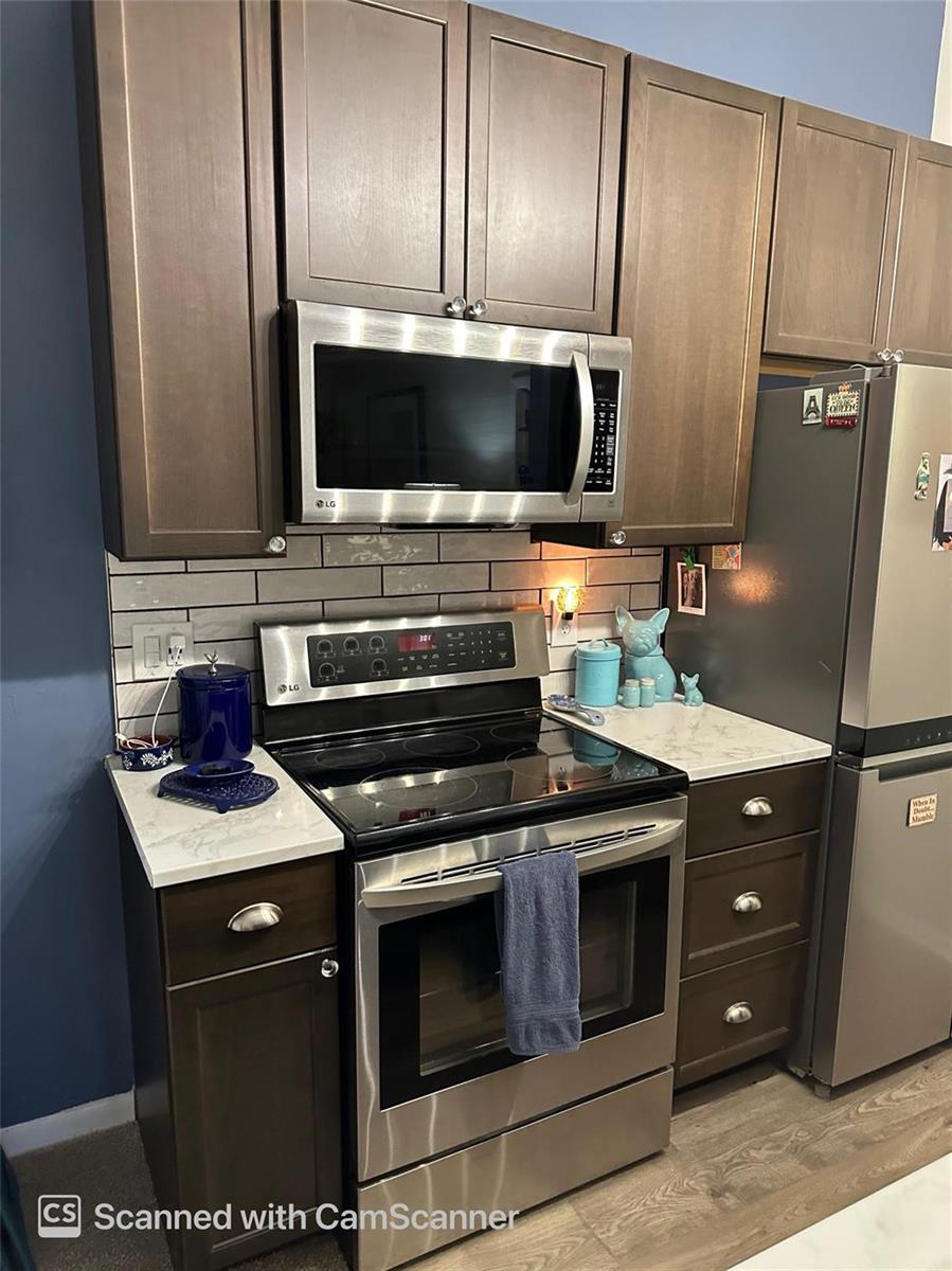 A kitchen features dark wood cabinets, stainless steel appliances, and a light-colored stone countertop — 6512 Chasewood Drive # H, Jupiter FL 33458, JUPITER, FL