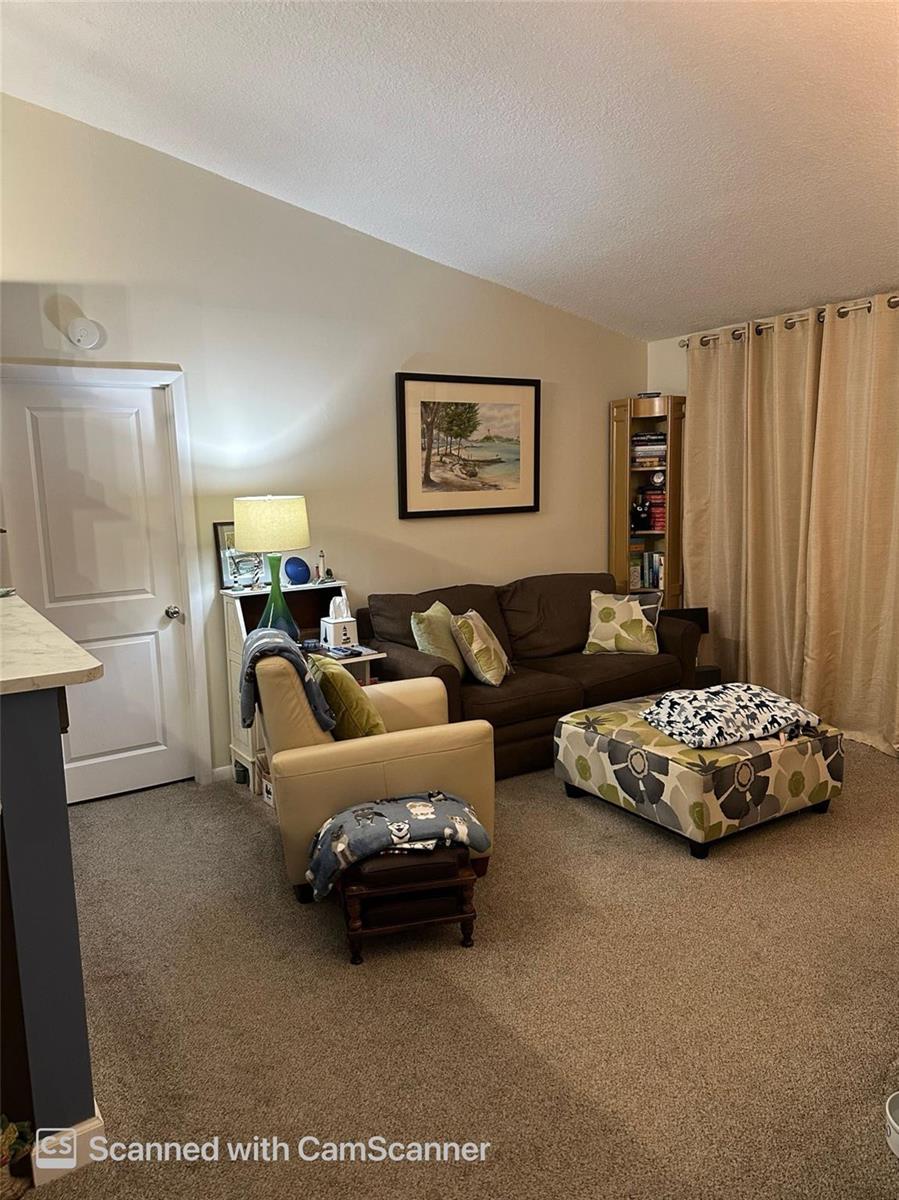 A living room features a brown sofa, a cream armchair, a patterned ottoman, and carpeted flooring — 6512 Chasewood Drive # H, Jupiter FL 33458, JUPITER, FL