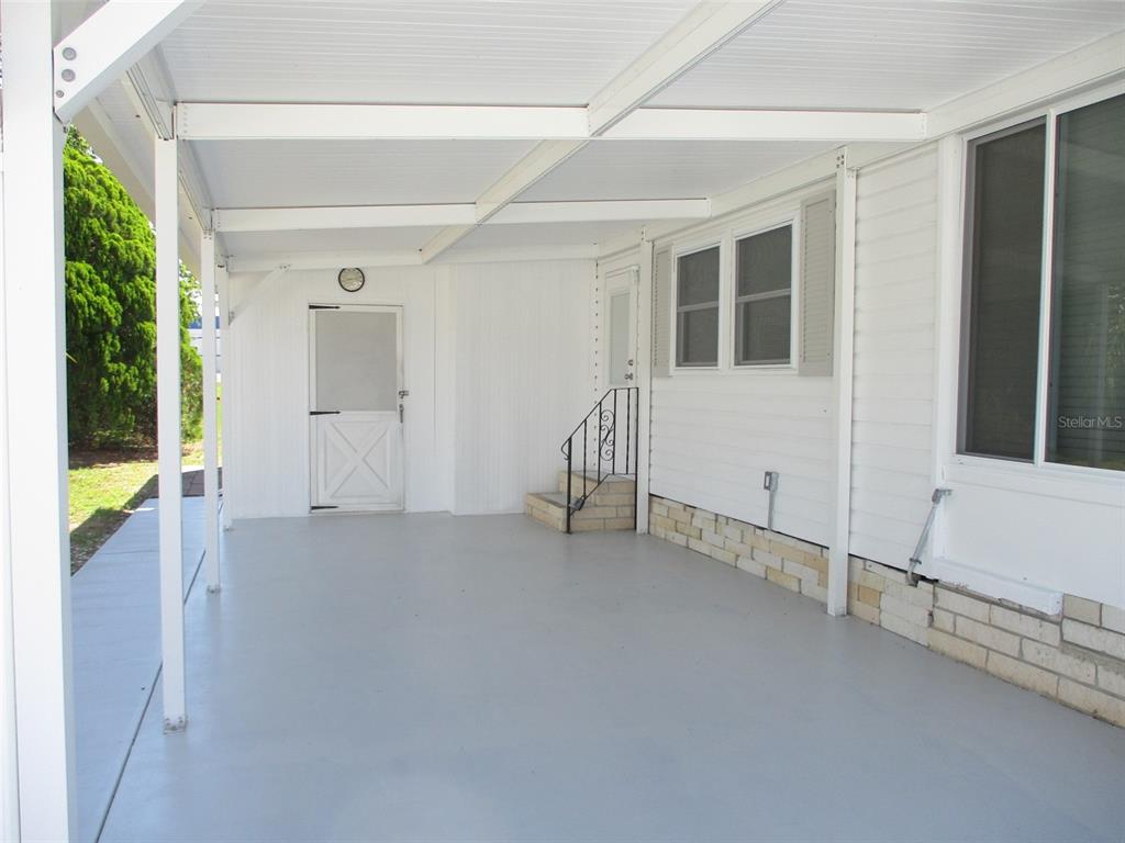 A covered concrete patio features white siding, a screen door, and steps leading to an entrance — 3734 CASTLE DRIVE, ZEPHYRHILLS, FL
