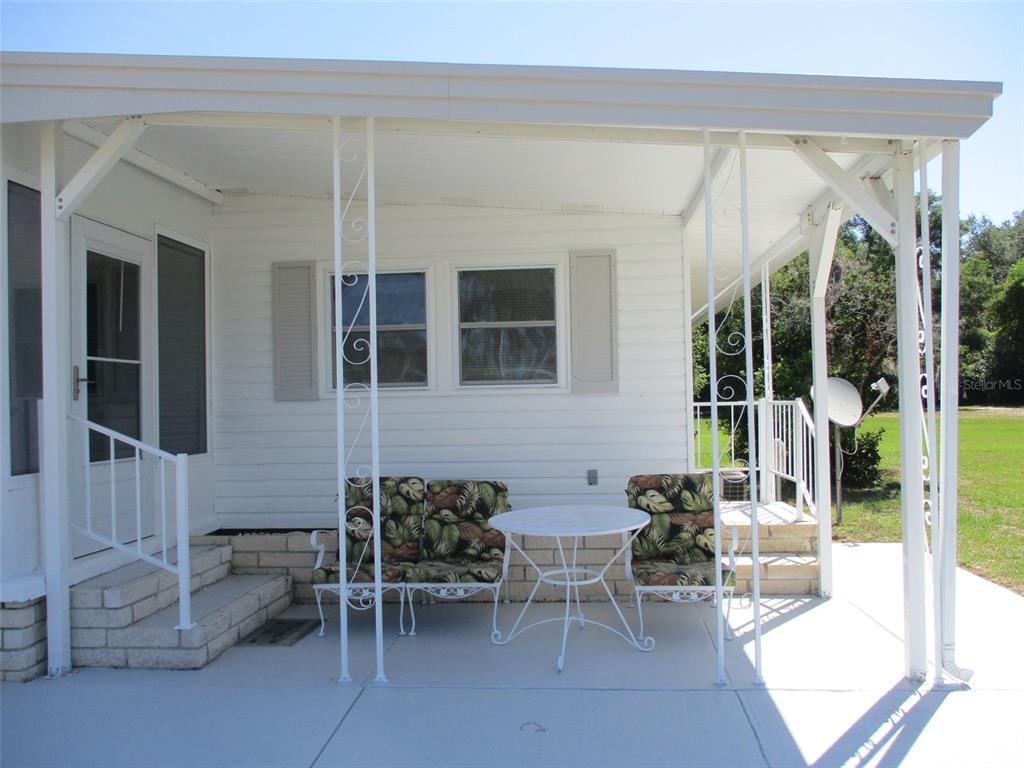 A white mobile home features a covered patio with metal railings and outdoor furniture — 3734 CASTLE DRIVE, ZEPHYRHILLS, FL