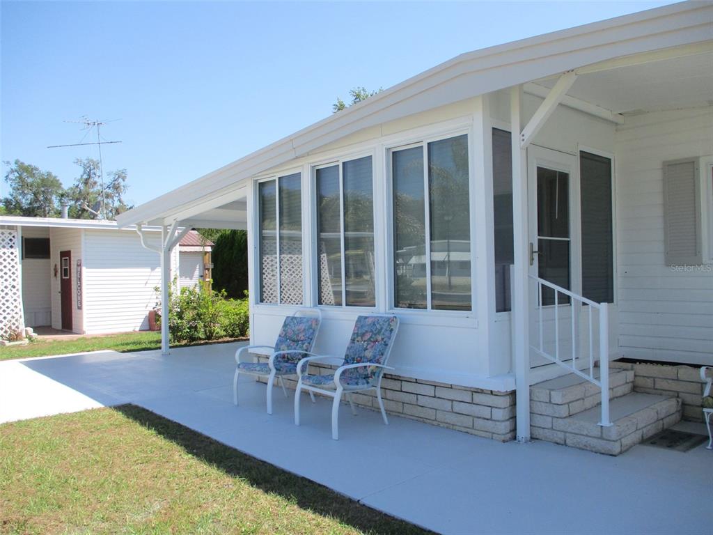 A white mobile home features a covered concrete patio, large windows, and a small staircase — 3734 CASTLE DRIVE, ZEPHYRHILLS, FL