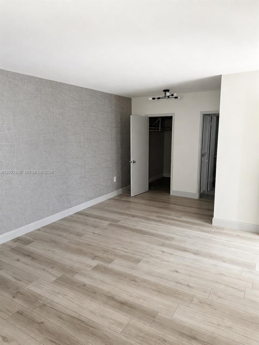 A bedroom features light wood-look flooring, a gray geometric accent wall, and two open doorways — 500 13th St # 7, Miami Beach FL 33139, MIAMI BEACH, FL