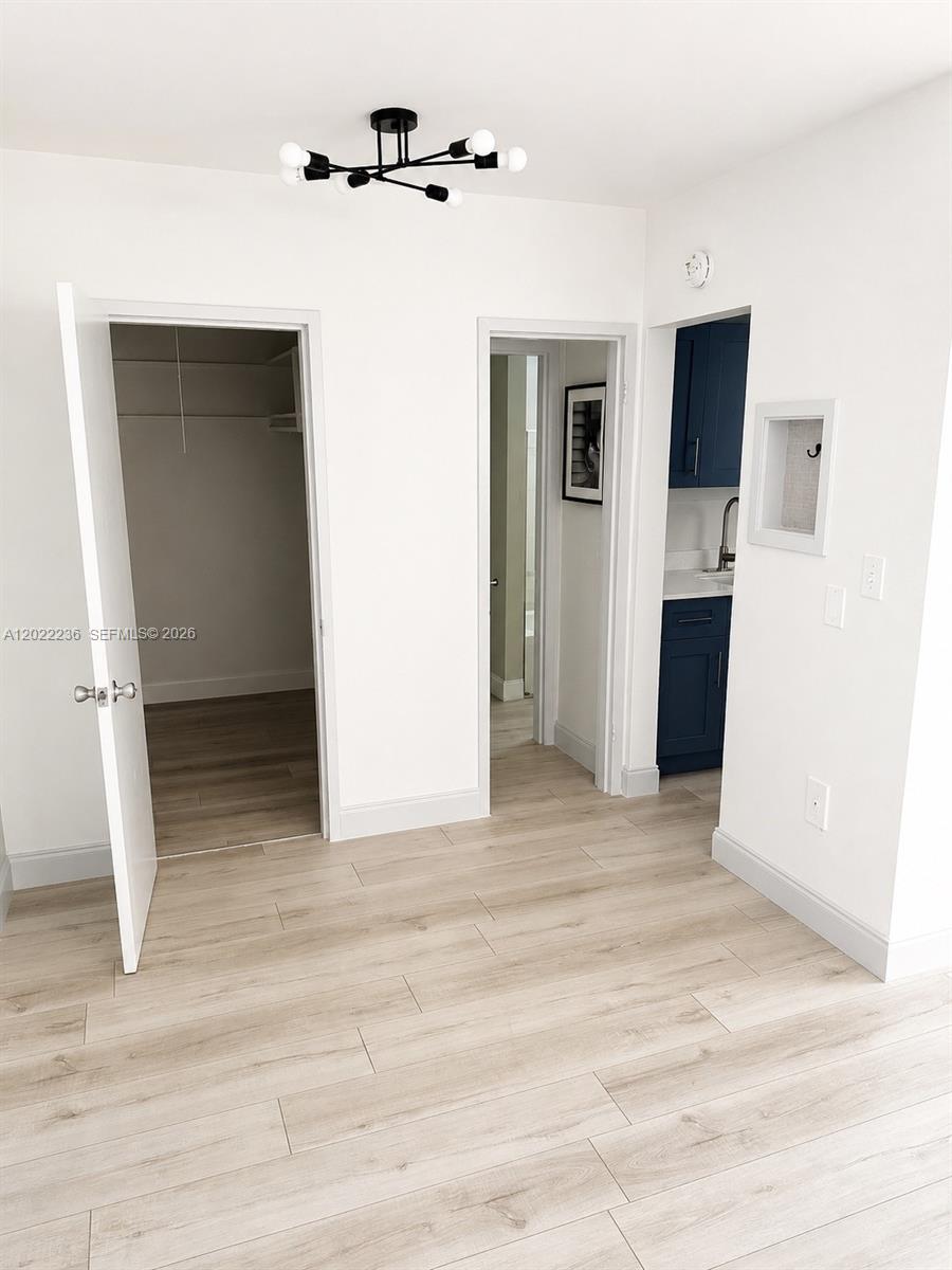 A room with light wood-look flooring features two doorways and a small blue kitchenette area — 500 13th St # 7, Miami Beach FL 33139, MIAMI BEACH, FL