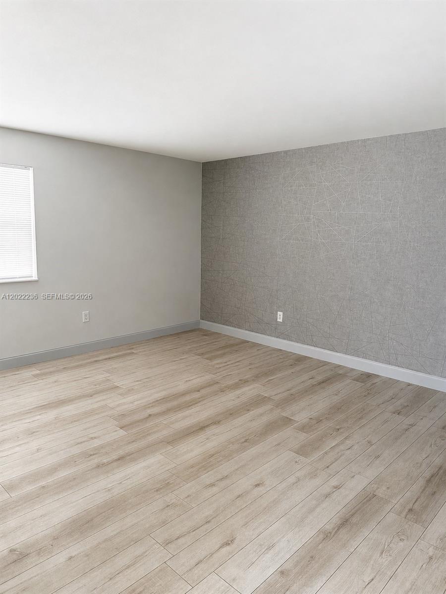 An empty room features light wood-look flooring, gray walls, and a geometric-patterned accent wall — 500 13th St # 7, Miami Beach FL 33139, MIAMI BEACH, FL