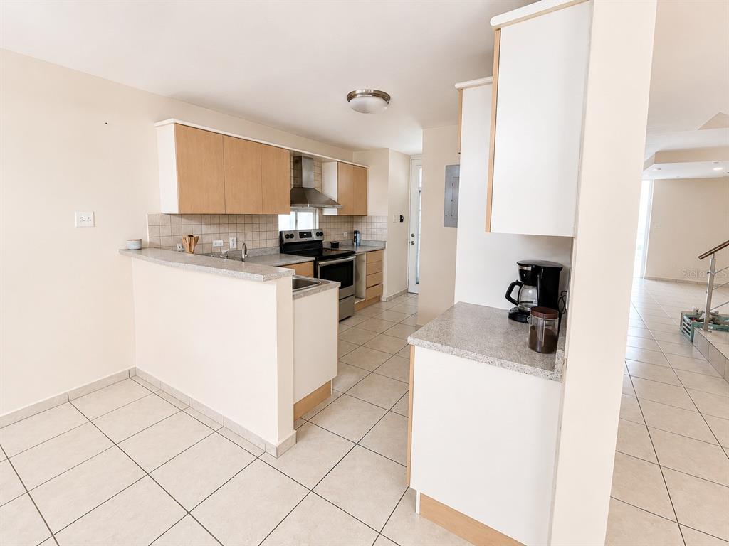 A kitchen features light wood cabinets, gray countertops, tile flooring, and a breakfast bar — L-143 URB PALACIOS DEL PR CALLE PACIFICO, JUANA DIAZ, PR