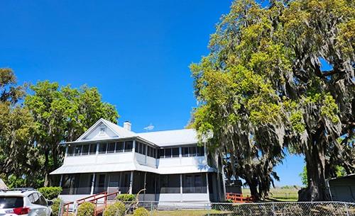 A two-story white house with a wrap-around porch stands beside a large moss-draped tree — 3650 LAKE TOHOPEKALIGA ROAD, ST CLOUD, FL