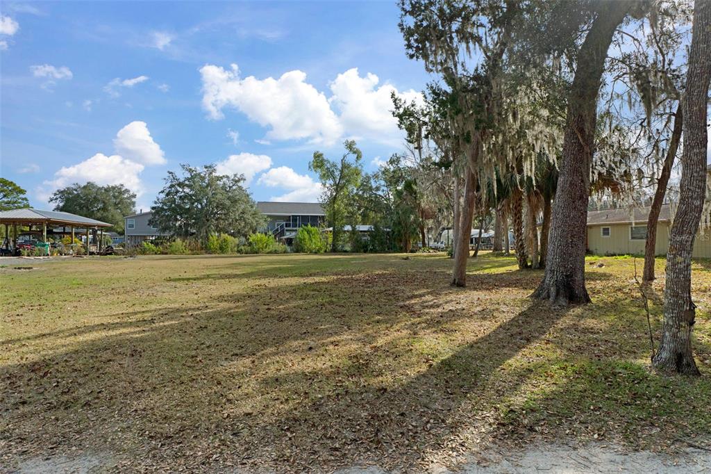 A large, grassy vacant lot features scattered trees and neighboring houses under a blue sky — 5799 S KINGDOM TERRACE, HOMOSASSA, FL