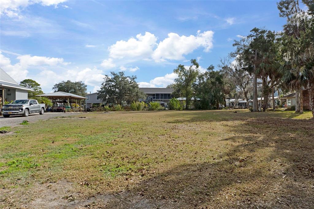 A wide, grassy vacant lot features a gravel driveway, a metal carport, and surrounding trees — 5799 S KINGDOM TERRACE, HOMOSASSA, FL