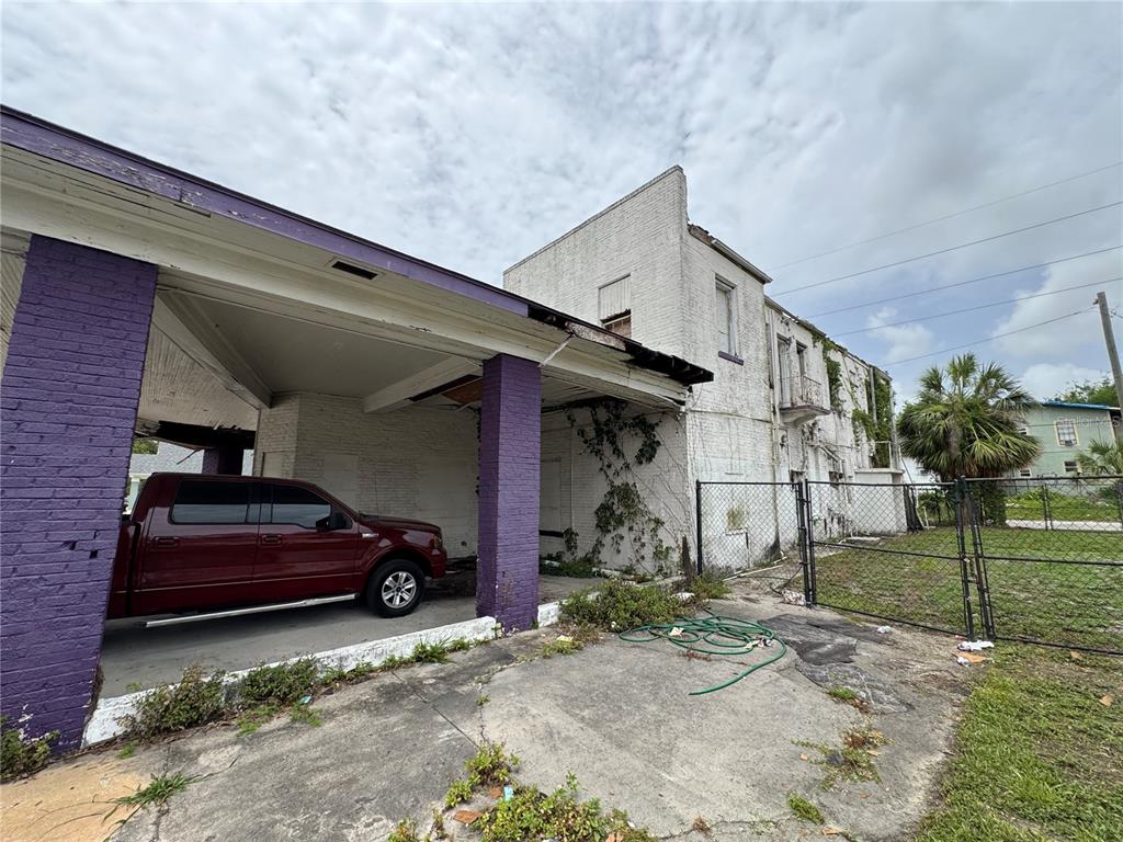 A red pickup truck is parked under a purple-pillared carport attached to a weathered building — 2804 E COLUMBUS DRIVE, TAMPA, FL