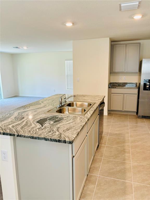 A kitchen island with a granite countertop and double sink sits in a tiled room — 13649 WHISKEY DAISY DRIVE, DADE CITY, FL