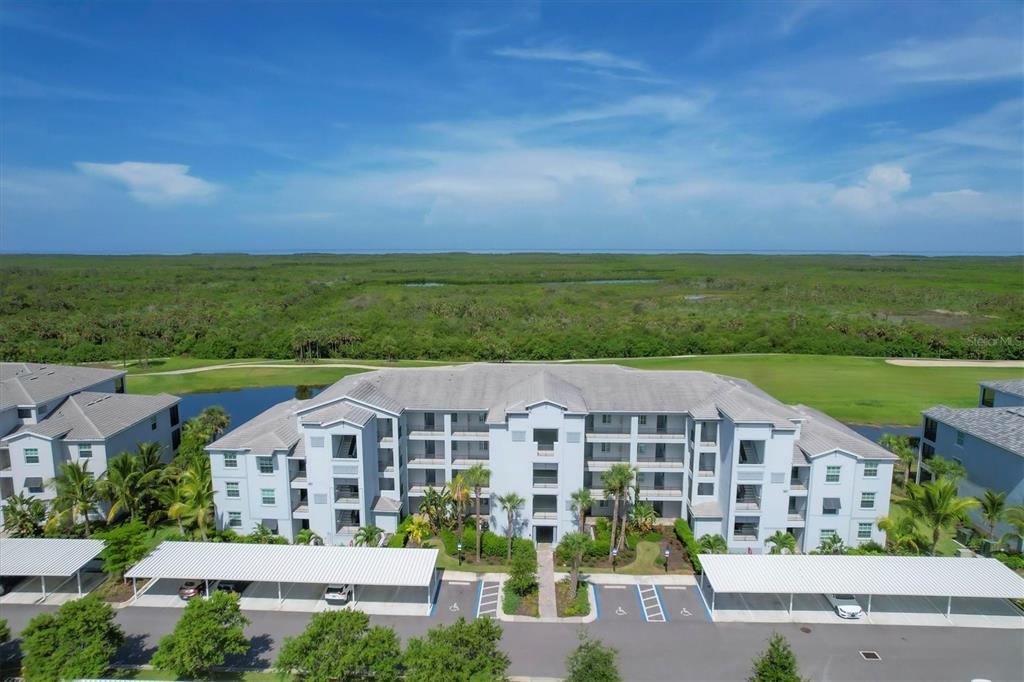 An aerial view of a multi-story apartment building with covered parking and surrounding green space — 14071 HERITAGE LANDING BOULEVARD UNIT 326, PUNTA GORDA, FL