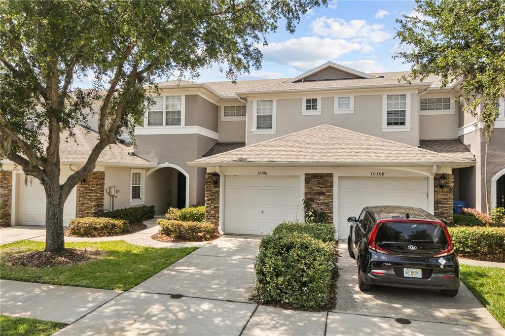 A two-story townhouse exterior features beige stucco, stone accents, and two attached garages — 10306 STONE MOSS AVENUE, TAMPA, FL