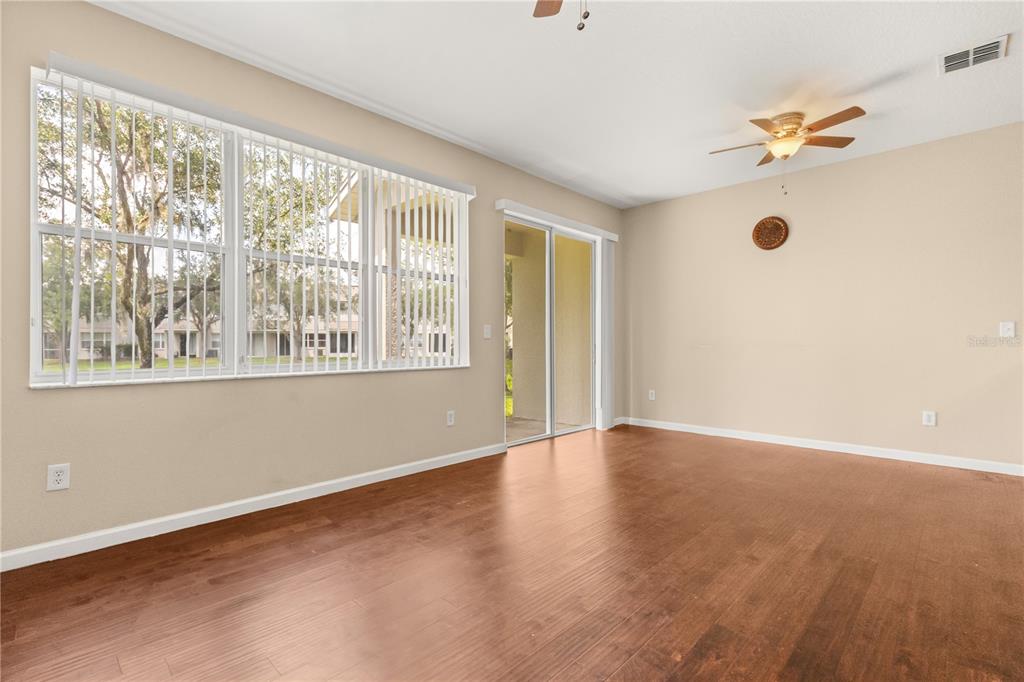 An empty living room features wood-look flooring, large windows, and a sliding glass door — 10306 STONE MOSS AVENUE, TAMPA, FL