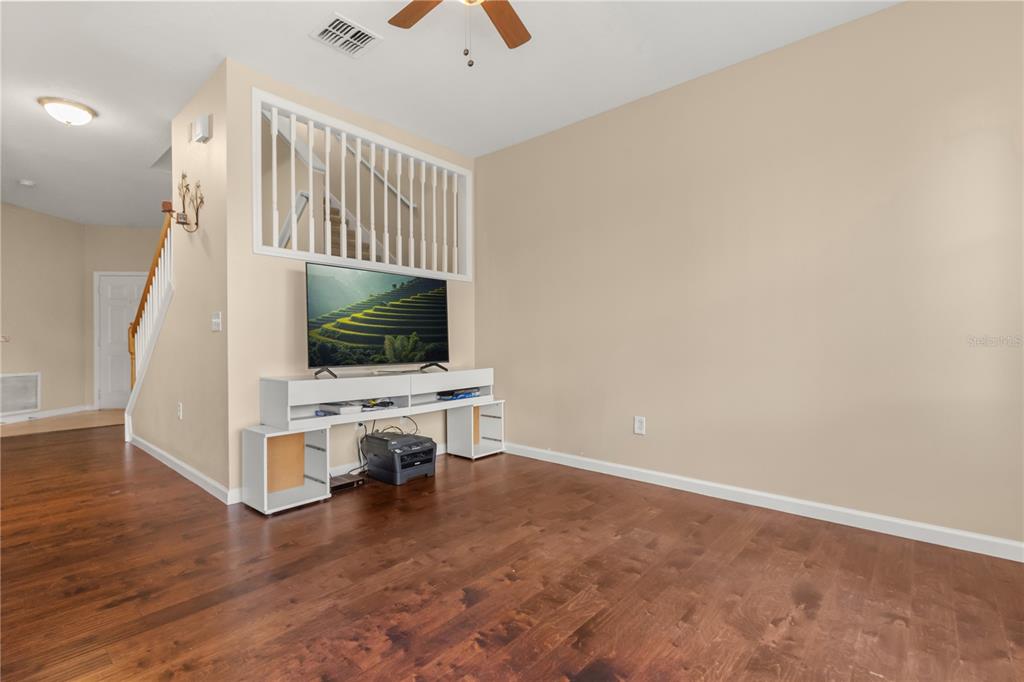 A living room features hardwood floors, a white media console, and a staircase with railings — 10306 STONE MOSS AVENUE, TAMPA, FL