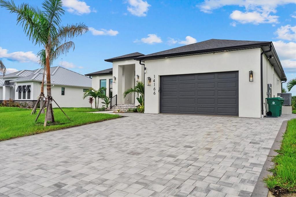 A modern, single-story house with a paved driveway, a two-car garage, and a palm tree — 14166 FORT WORTH CIRCLE, PORT CHARLOTTE, FL