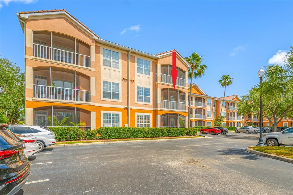An exterior view of a multi-story apartment building with a red arrow pointing to a balcony — 5000 CULBREATH KEY WAY UNIT 1-201, TAMPA, FL
