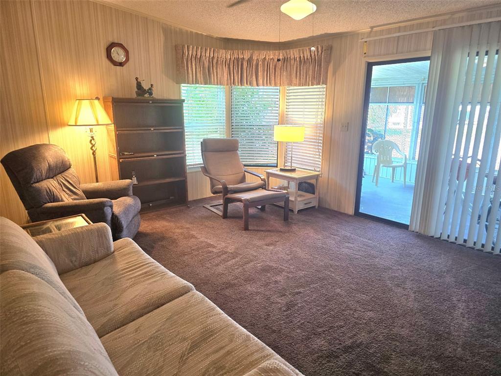 A living room features brown carpeting, a sofa, a recliner, a bookshelf, and a sliding door — 379 TOWNBRIDGE DRIVE, HAINES CITY, FL