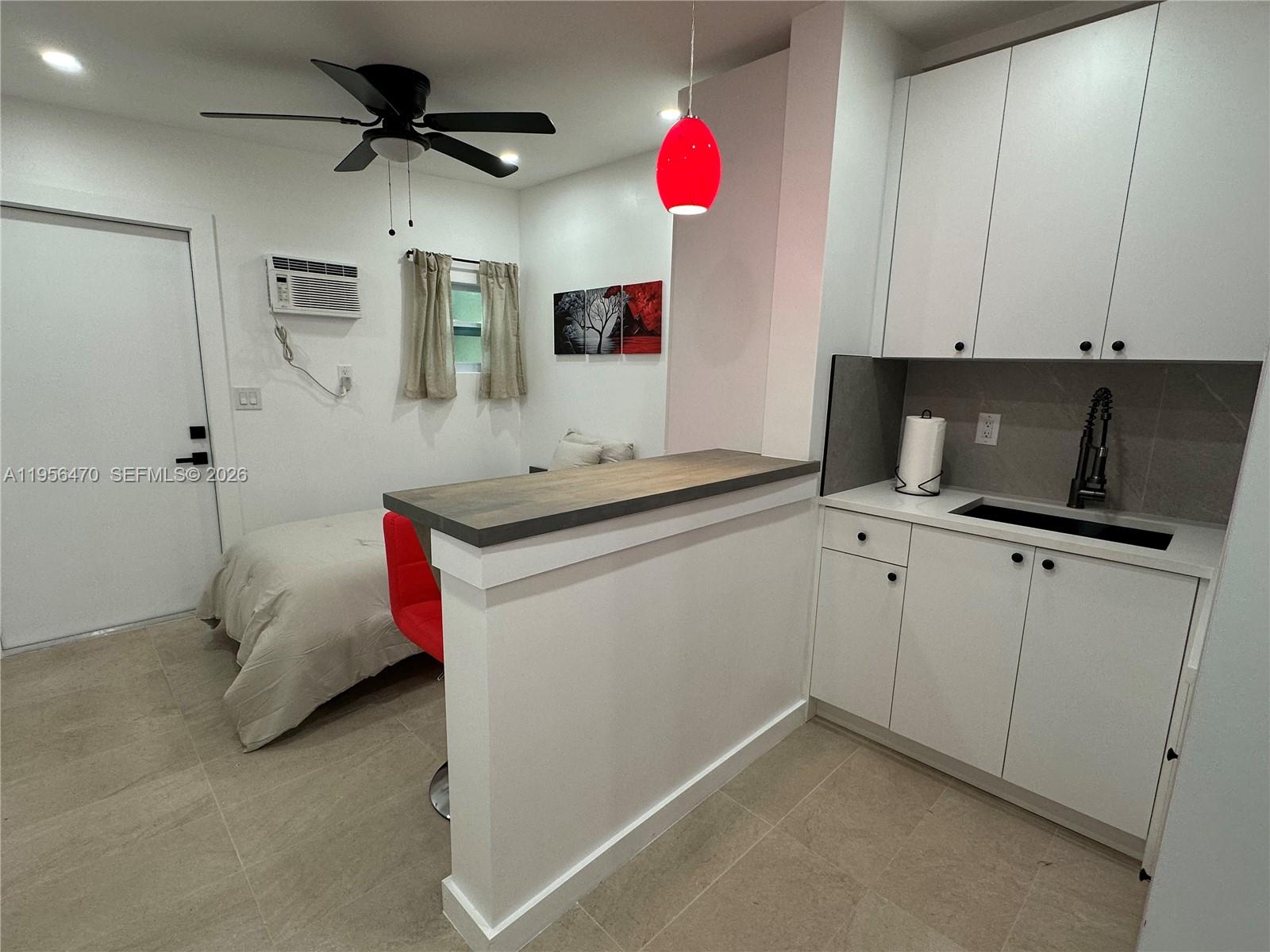 A studio apartment features a kitchenette with white cabinets, a breakfast bar, and a bed — 18481 SW 208th St # 18481, Miami FL 33187, MIAMI, FL