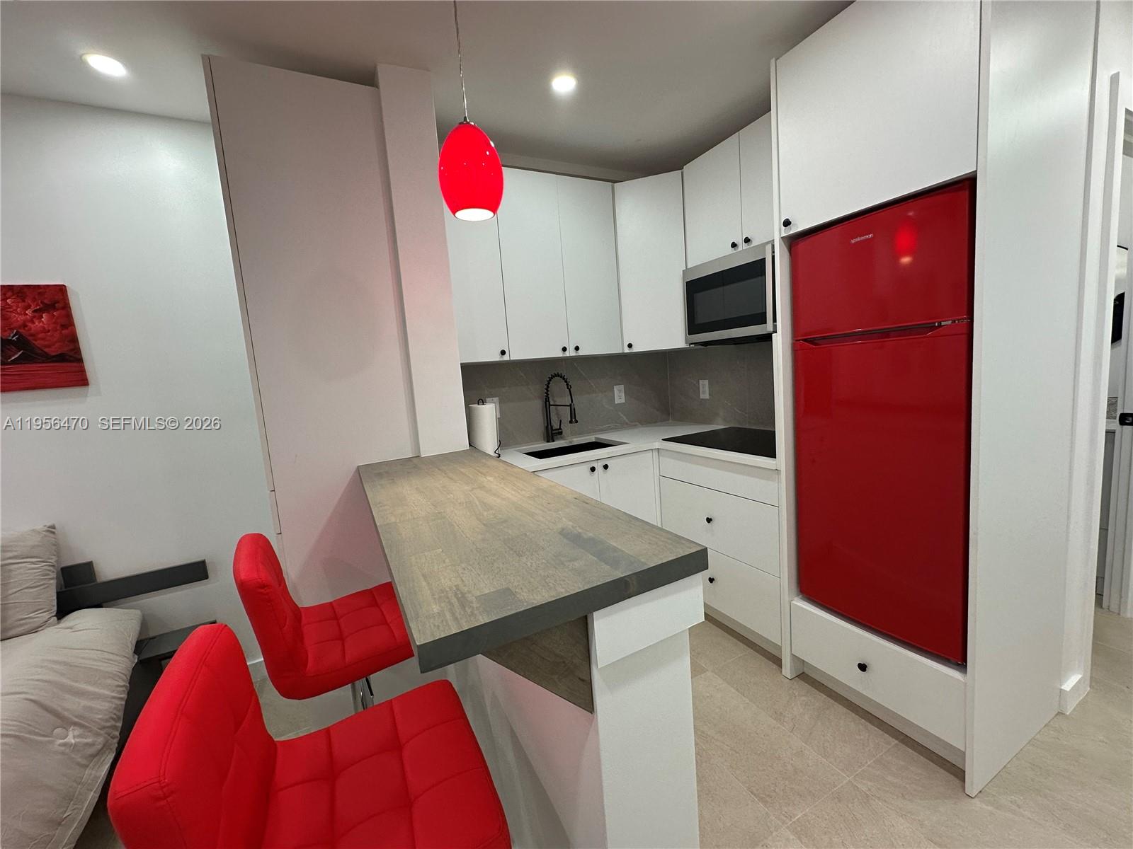 A small kitchen features white cabinets, a red refrigerator, and a wooden breakfast bar — 18481 SW 208th St # 18481, Miami FL 33187, MIAMI, FL
