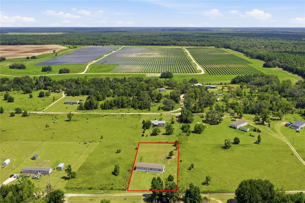 An aerial view shows a rectangular lot with a house outlined in red near a solar farm — 9831 NE 100TH STREET, ARCHER, FL