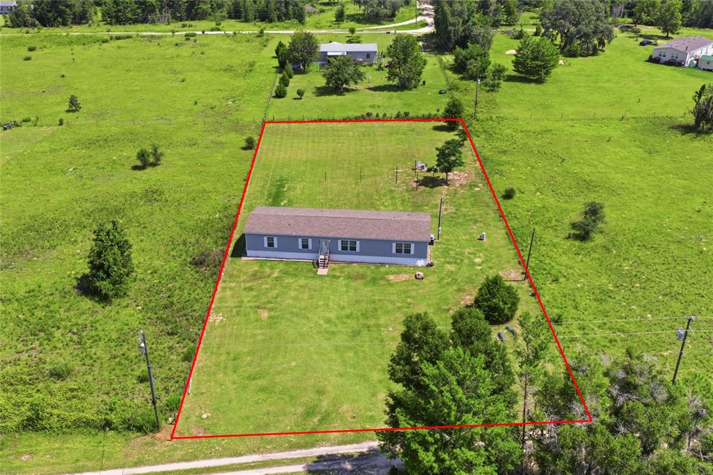 An aerial view shows a rectangular property lot containing a single-story house with a red outline — 9831 NE 100TH STREET, ARCHER, FL