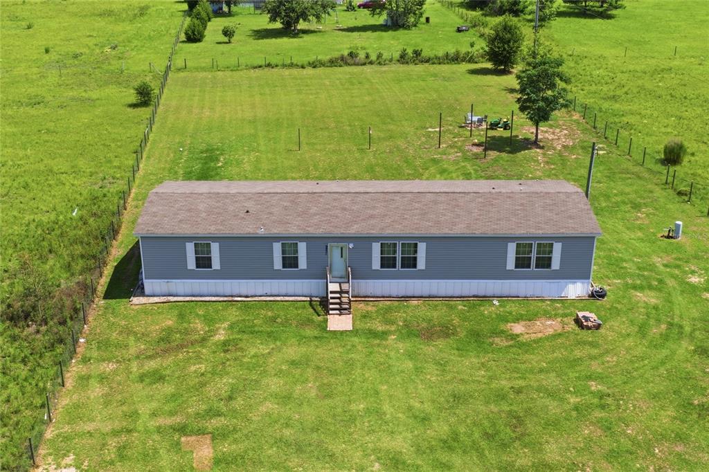 An aerial view shows a single-story manufactured home with gray siding on a grassy lot — 9831 NE 100TH STREET, ARCHER, FL