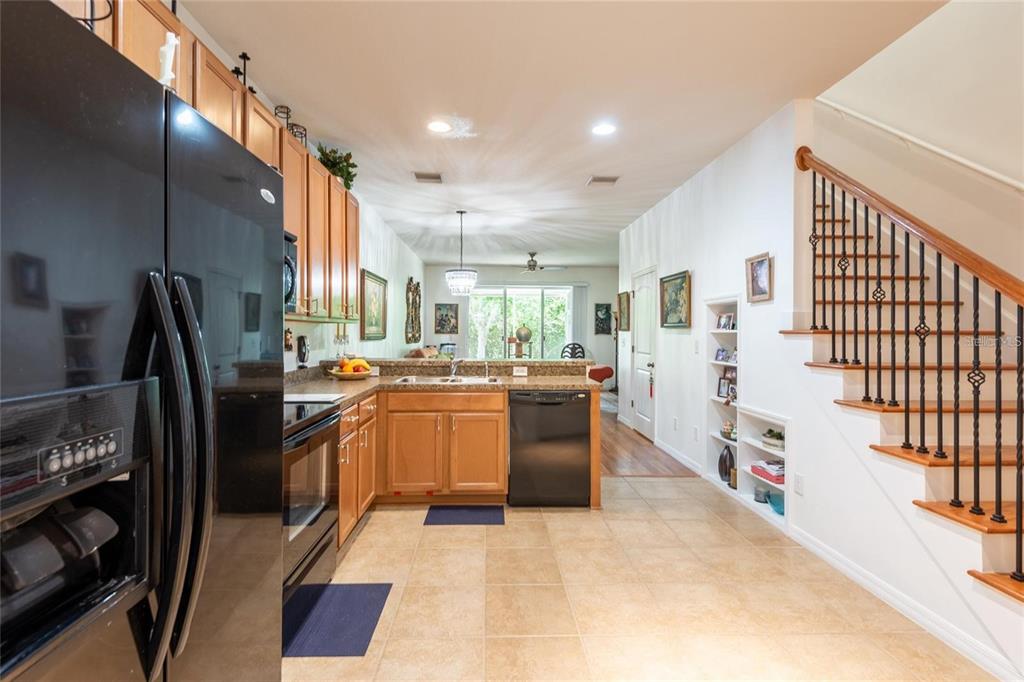 A kitchen with wood cabinets, black appliances, and tile floors next to an open staircase — 8931 TURNSTONE HAVEN PLACE, TAMPA, FL