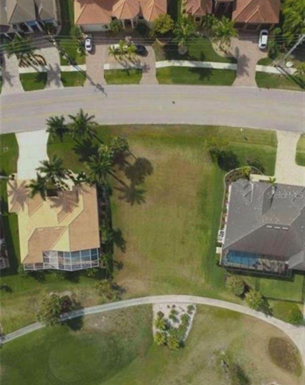 An aerial view shows a vacant residential lot situated between two houses near a golf course — 272 MADRID BOULEVARD, PUNTA GORDA, FL