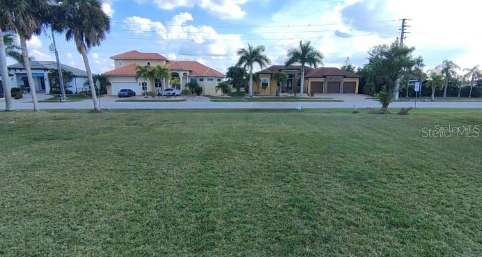An empty grassy lot faces a street lined with several large suburban houses and palm trees — 272 MADRID BOULEVARD, PUNTA GORDA, FL