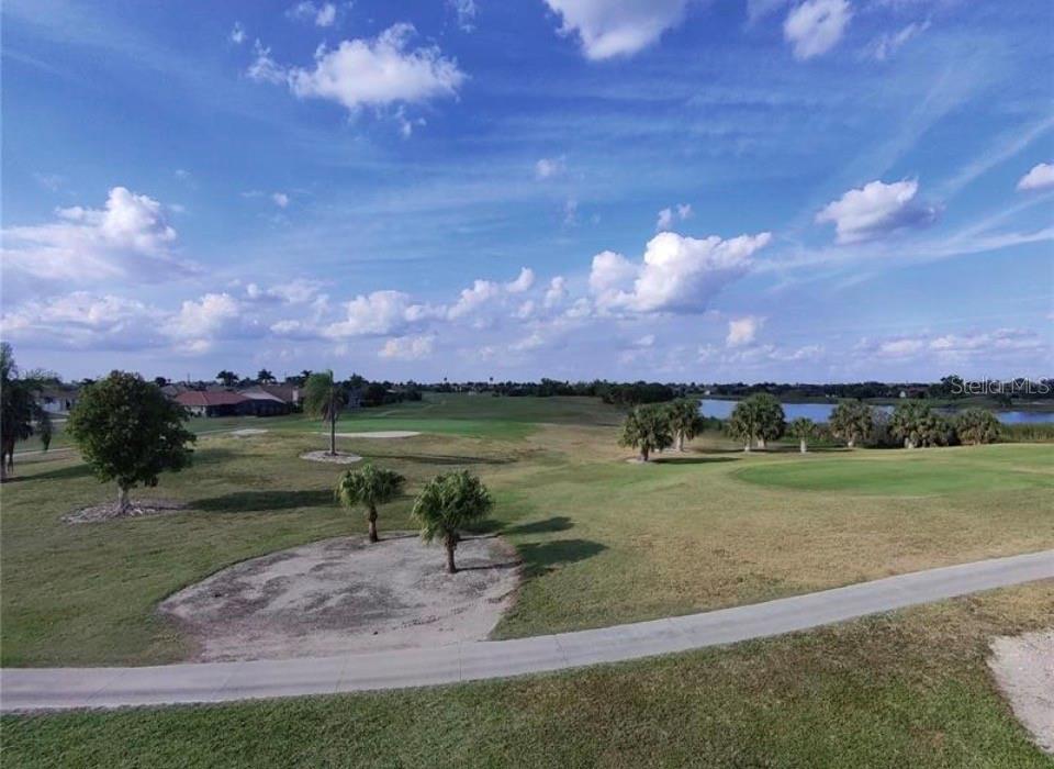 A view of a golf course with palm trees, a pond, and houses in the distance — 272 MADRID BOULEVARD, PUNTA GORDA, FL