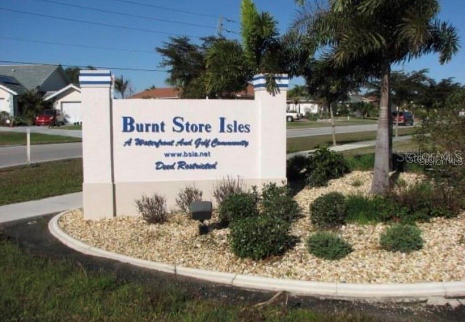 A sign for Burnt Store Isles stands in a landscaped garden bed near a street — 272 MADRID BOULEVARD, PUNTA GORDA, FL