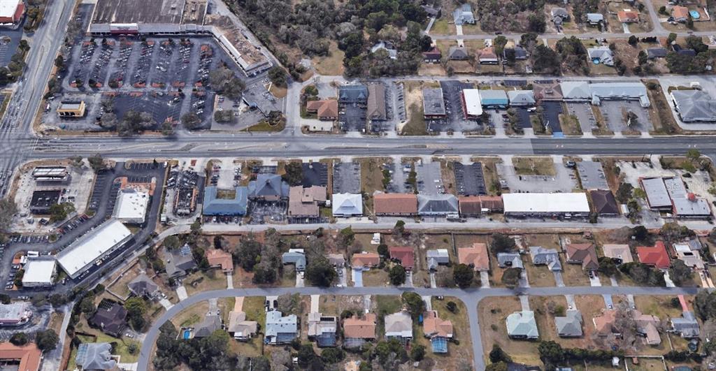 This aerial view shows a commercial strip mall with parking lots adjacent to residential neighborhoods — 11001 SPRING HILL DRIVE, SPRING HILL, FL