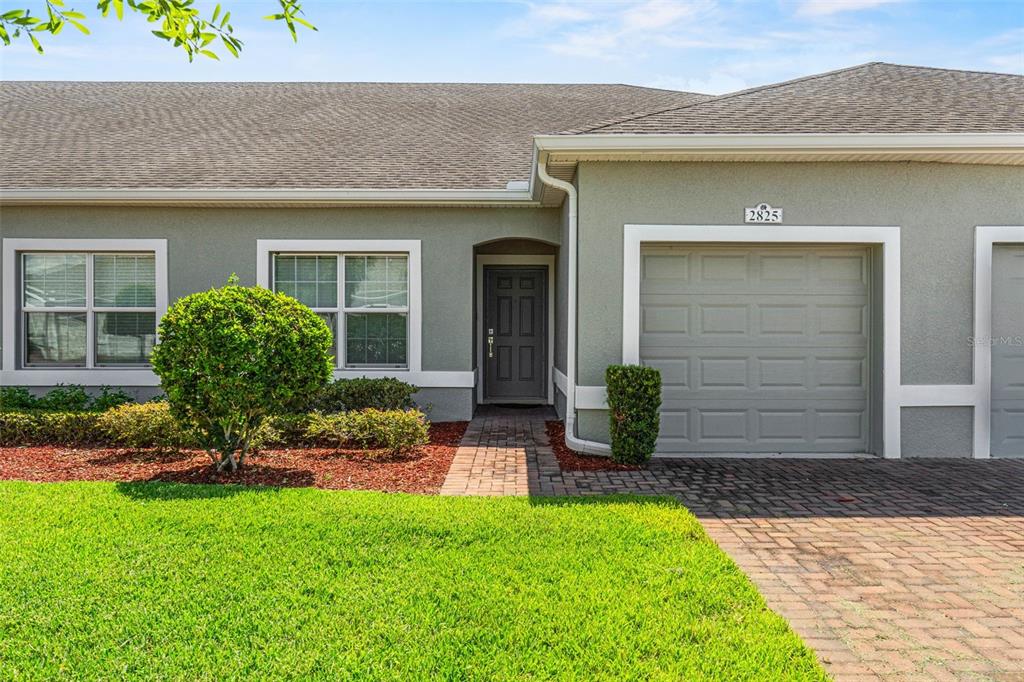 The exterior of a single-story home features a gray stucco facade, a garage, and landscaping — 2825 ATTWATER LOOP, WINTER HAVEN, FL