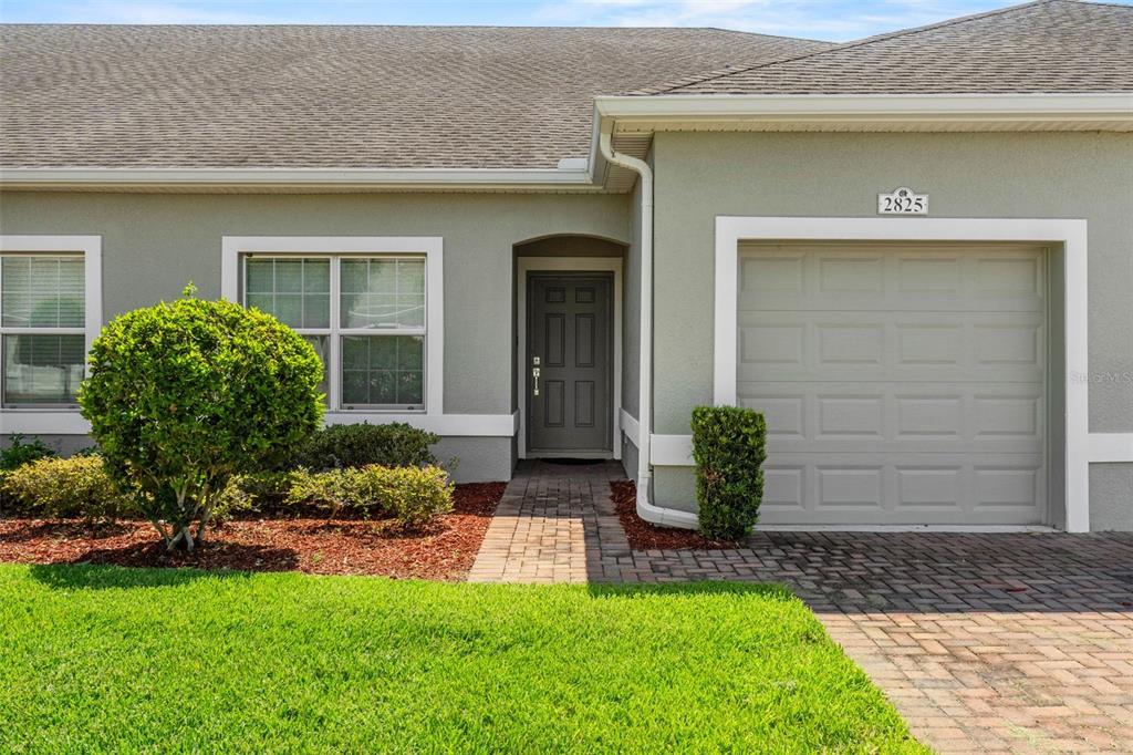 A single-story house exterior features a gray garage, a dark front door, and landscaping — 2825 ATTWATER LOOP, WINTER HAVEN, FL