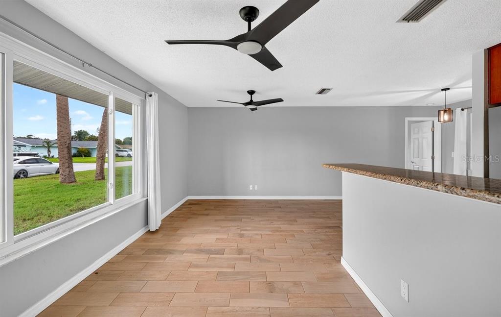 An empty room with wood-look tile flooring, two ceiling fans, and a large window — 1309 SUWANEE ROAD, DAYTONA BEACH, FL