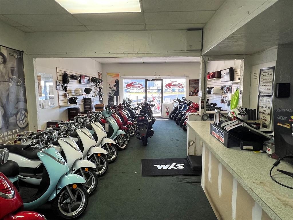 A showroom displays multiple scooters and motorcycles with parts on shelves and a service counter — 853 US-41-BYP UNIT 853, VENICE, FL