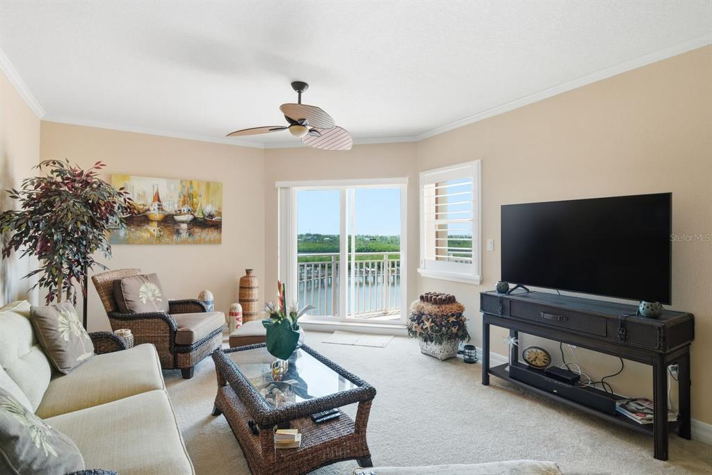 A living room features a sofa, wicker chair, glass-top coffee table, television, and balcony view — 4516 SEAGULL DRIVE UNIT 502, NEW PORT RICHEY, FL