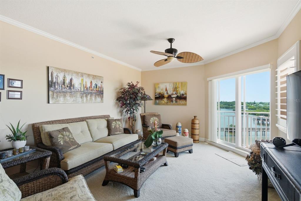 A living room features wicker furniture, a ceiling fan, and a balcony overlooking the water — 4516 SEAGULL DRIVE UNIT 502, NEW PORT RICHEY, FL